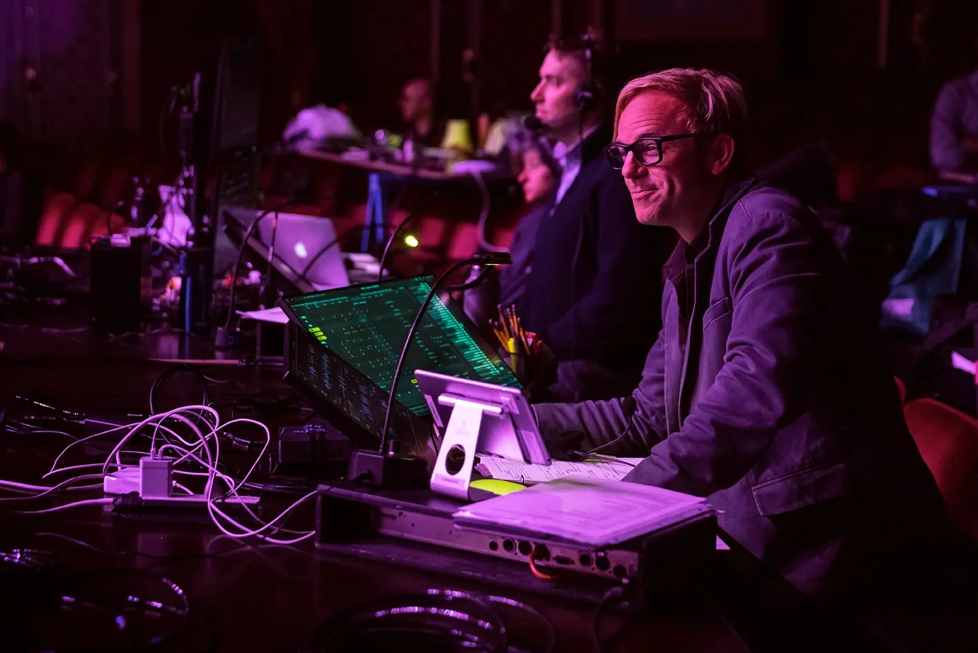Justin Townsend, lighting designer of Moulin Rouge! The Musical sitting at a lighting station inside the theatre, illuminated by purple lighting