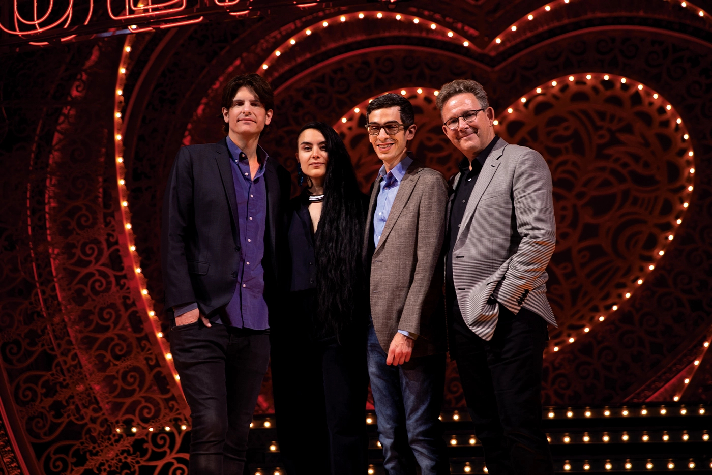 Alex Timbers (director), Sonya Tayeh (choreographer), Justin Levine (music arrangements), and John Logan (book) standing together on the Moulin Rouge! The Musical set