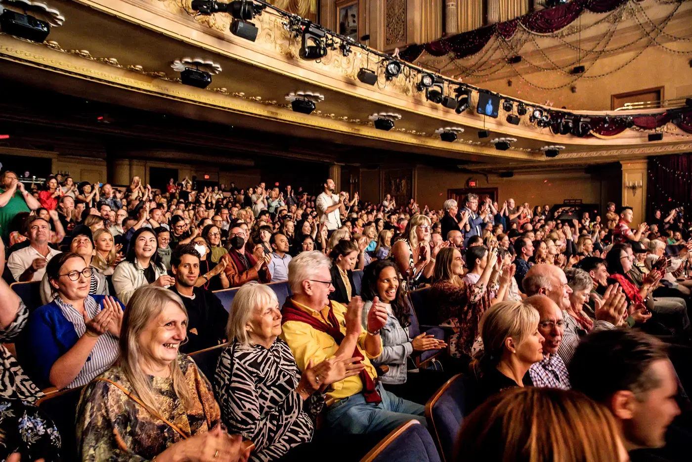 The audience at the end of a performance of Moulin Rouge! The Musical applauding the performance. Some are seen standing up while applauding.