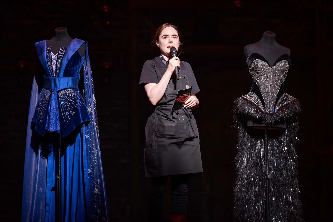 A crew member on stage showing off some of the show's costumes on stage during 'Get Technical! Behind the Curtain of Moulin Rouge! The Musical' on the West End.
