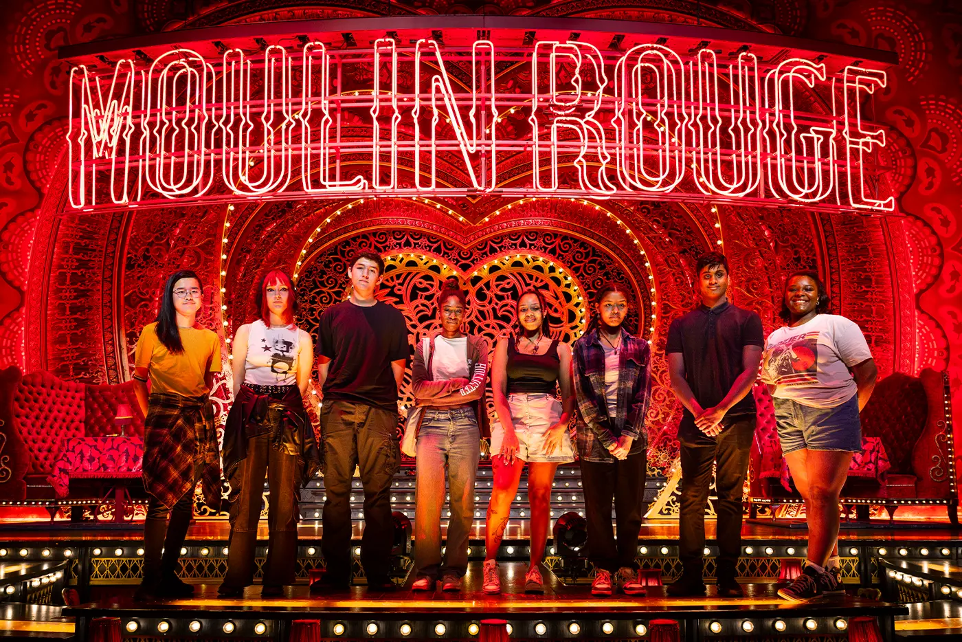 The students of the Get Technical Academy standing on stage under the 'MOULIN ROUE' neon sign. They are illuminated by red lighting.