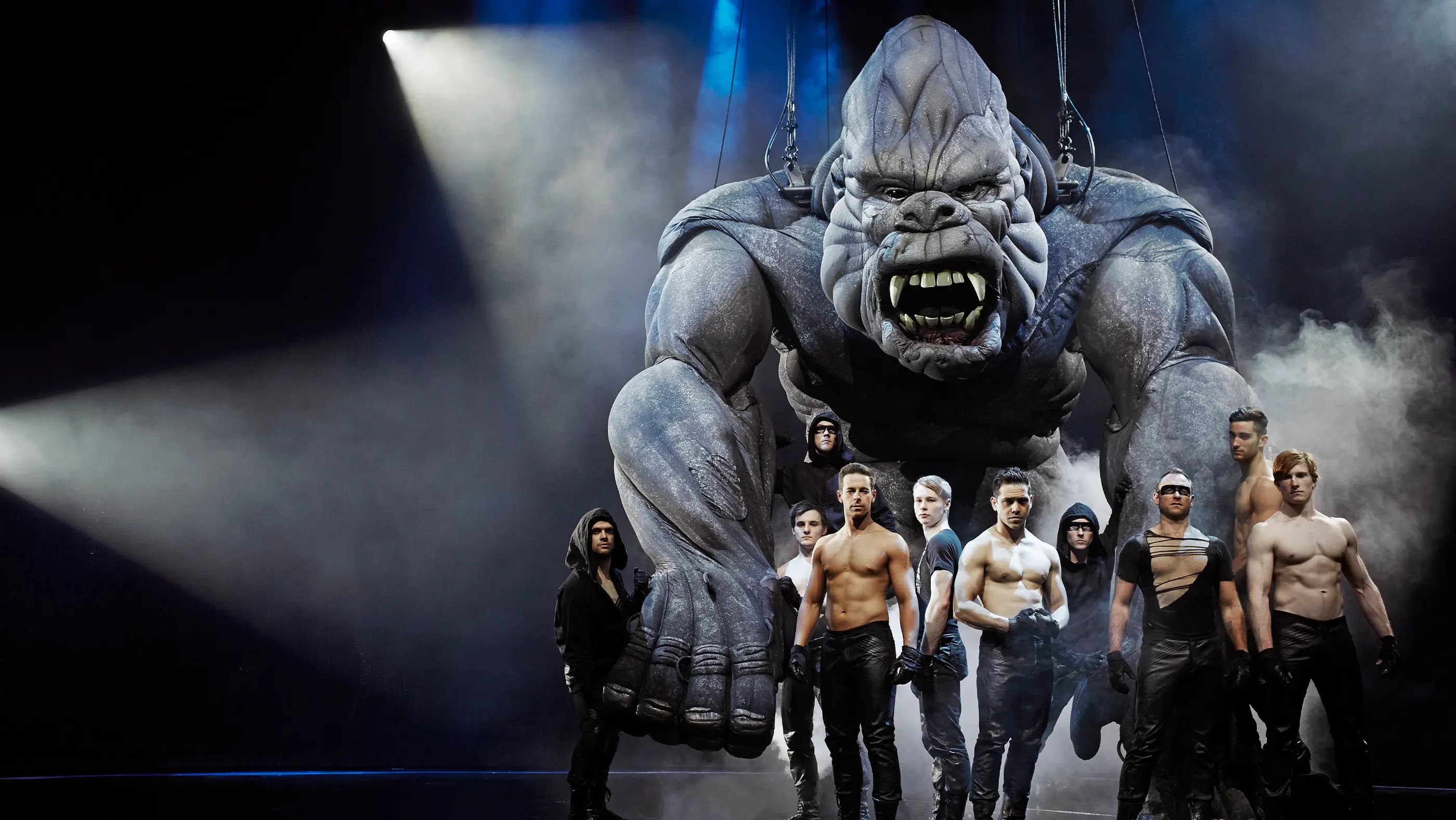 An enormous King Kong in the background with the Kings Men puppeteers standing in front shirtless.