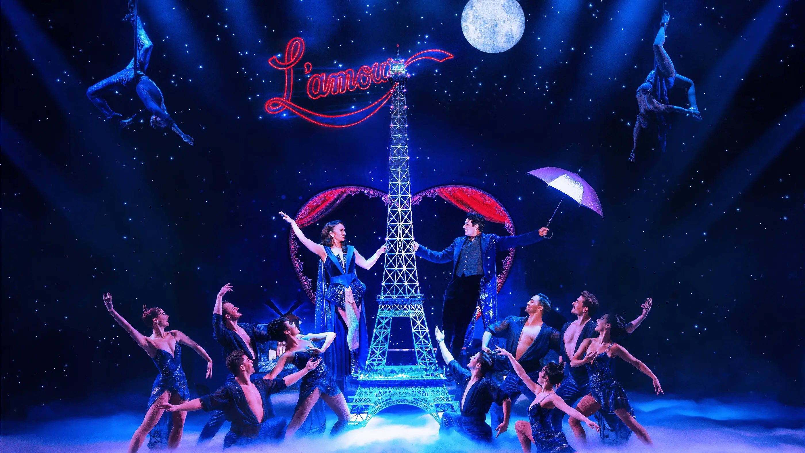 Scene from Moulin Rouge! The Musical Australia during “Elephant Love Medley,” with two main characters beside a central Eiffel Tower structure, one holding a sparkly umbrella, under starry lights and a glowing “L’amour” sign.