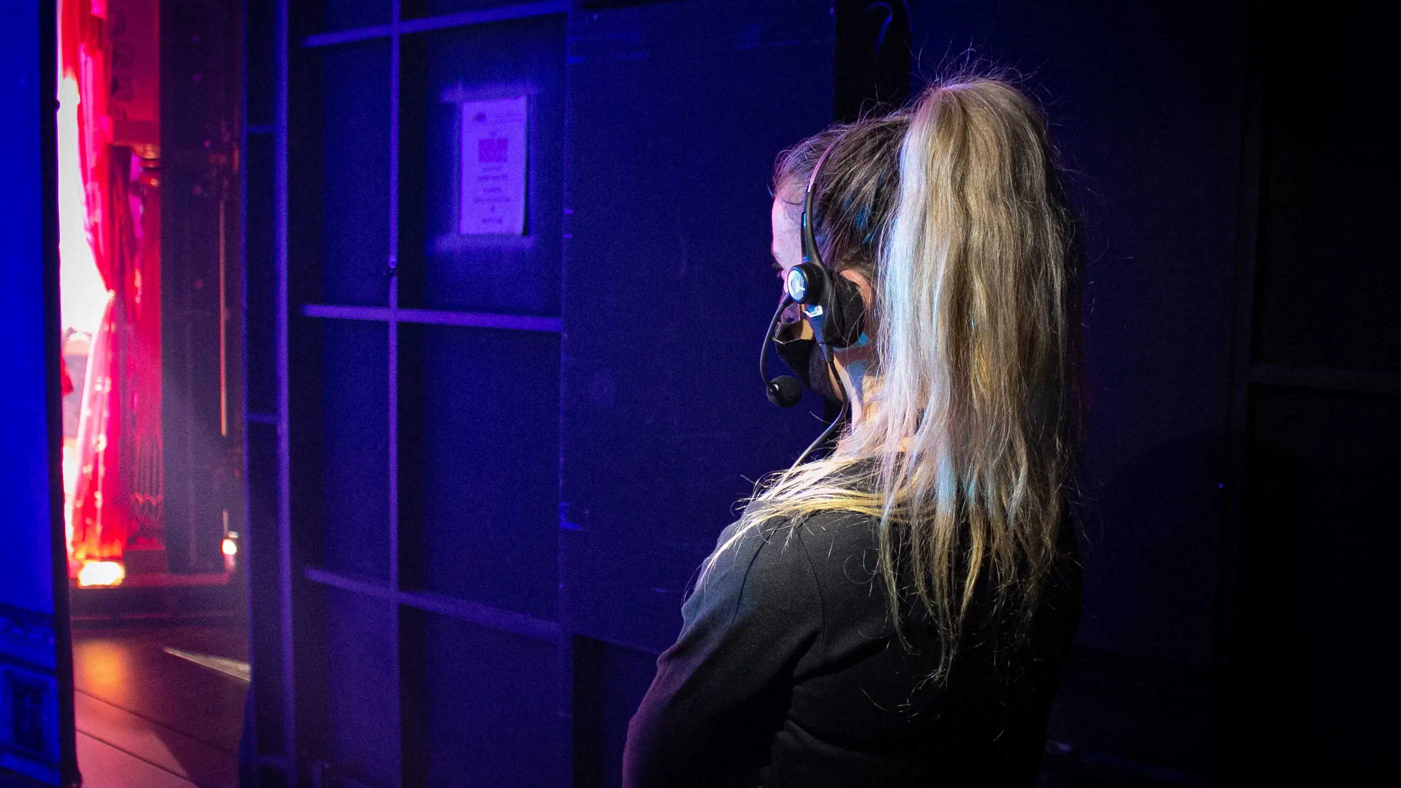 The Assistant Stage Manager of Moulin Rouge! The Musical looks onto the stage from the wings. She is wearing a headset with a microphone.