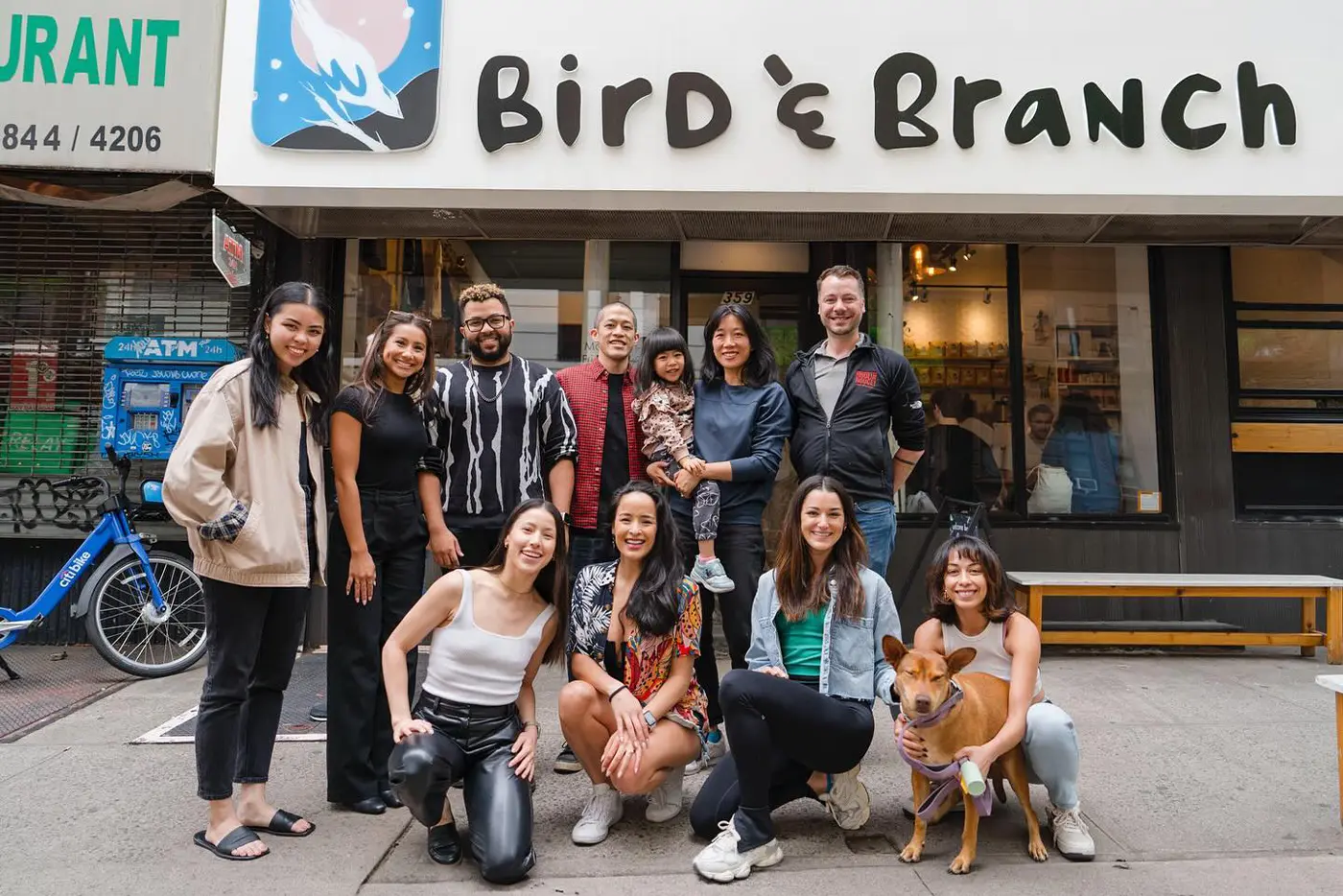 Moulin Rouge! The Musical company members standing outside a cafe with big lettering 'Bird & Branch'.