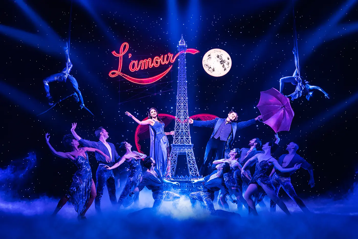 Scene from Moulin Rouge! The Musical Broadway during “Elephant Love Medley,” with two main characters beside a central Eiffel Tower structure, one holding a sparkly umbrella, under starry lights and a glowing “L’amour” sign.
