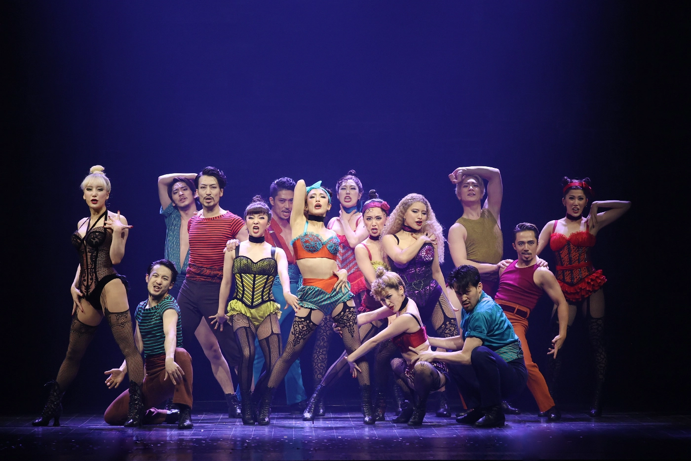 Scene from Moulin Rouge! The Musical Japan during “Backstage Romance,” featuring performers in vibrant theatrical costumes posed dramatically under stage lighting.