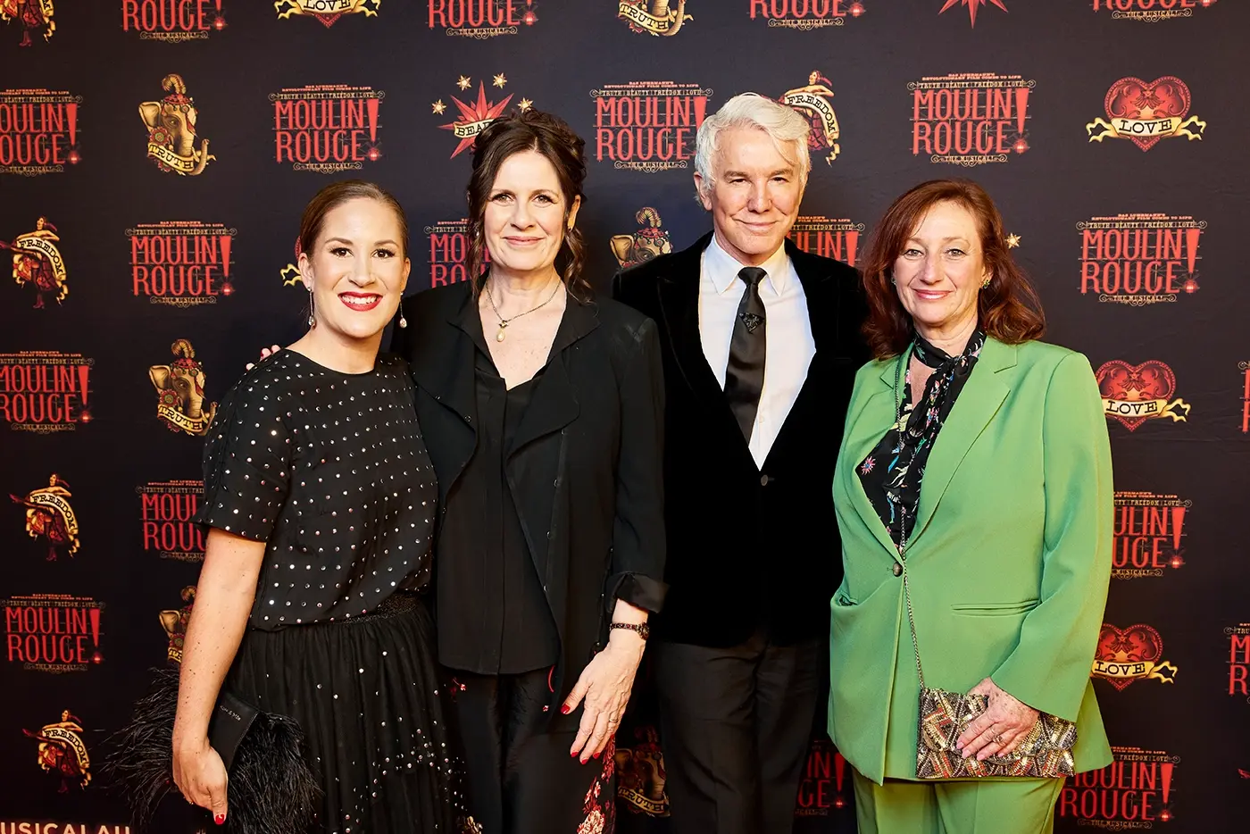 Julie Norman, Carmen Pavlovic, Baz Luhrmann, and Angela Dalton pose in front of a Moulin Rouge! The Musical media wall on opening night in Brisbane.