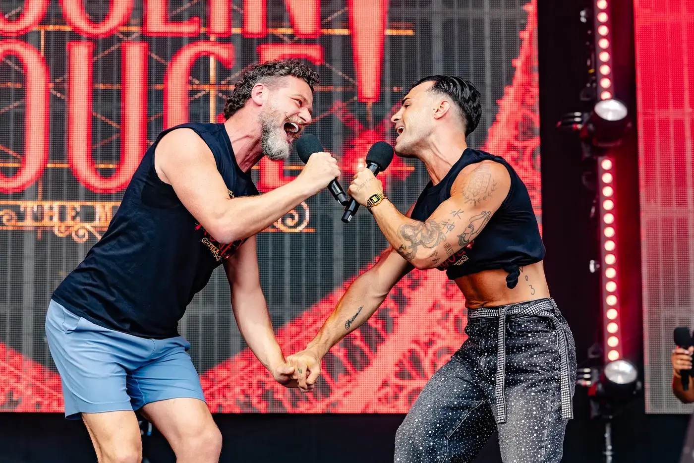 Two male performers from Moulin Rouge! The Musical holding hands while singing to each other on stage.