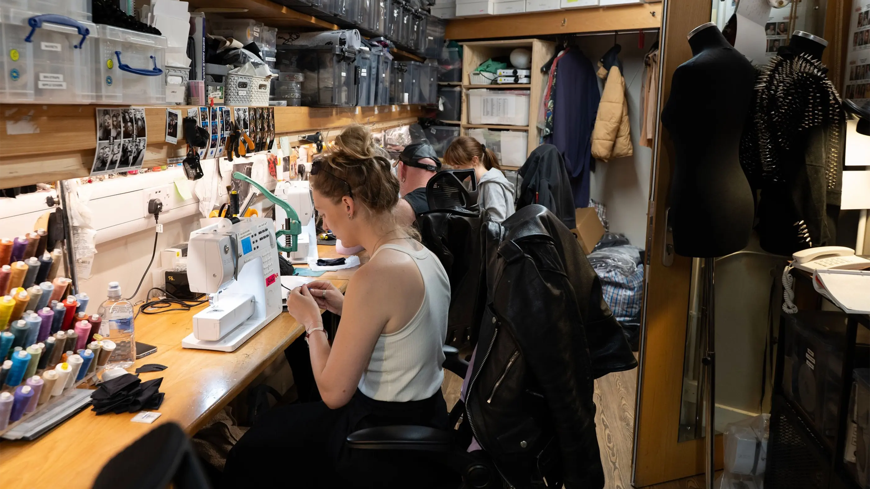 Some of the crew working backstage at Moulin Rouge! The Musical. In the foreground, a person is seen using a sewing machine to fix a costume piece.