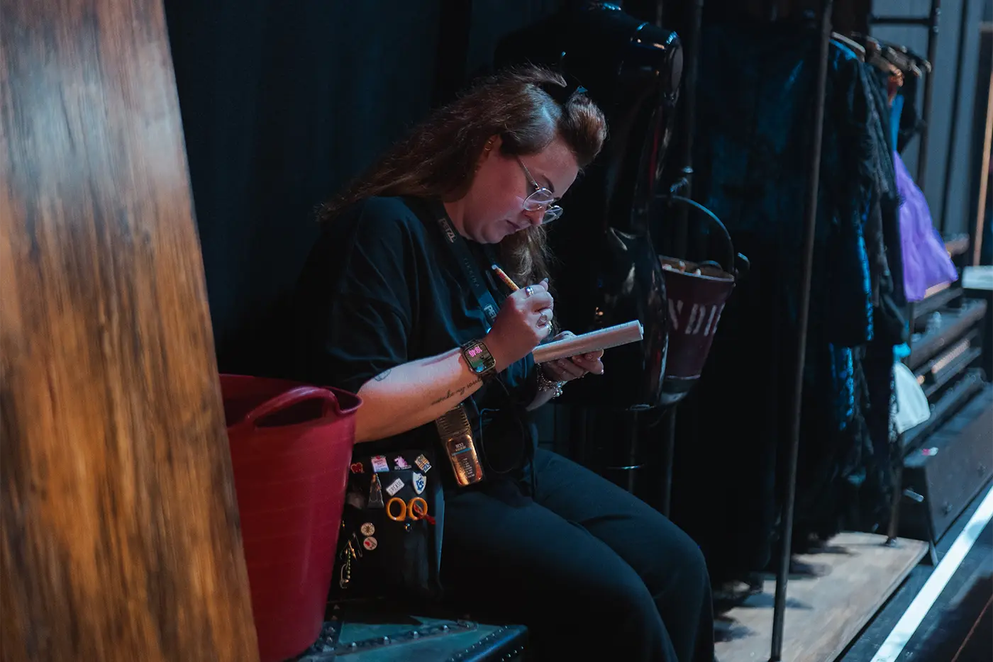A crew member backstage at Moulin Rouge! The Musical World Tour taking notes while sitting beside costumes hanging on a clothing rack