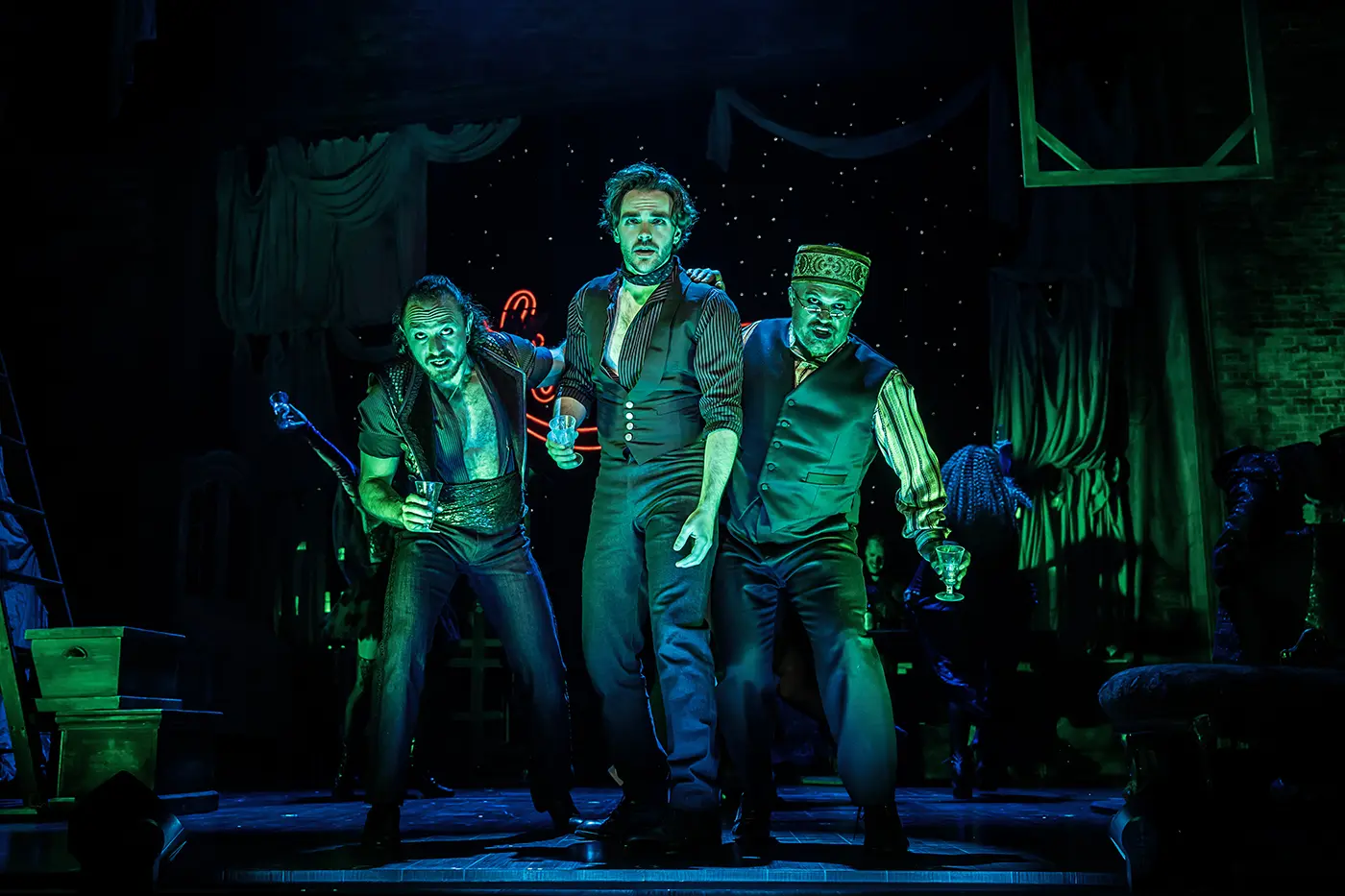 Santiago, Christian, and Toulouse-Lautrec standing together under green lighting from the 'Chandelier' scene in Moulin Rouge! The Musical World Tour.