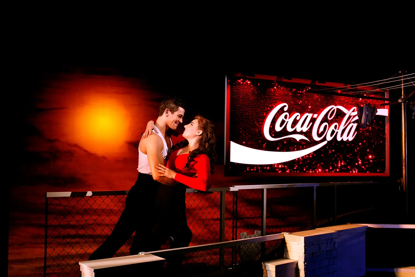Iconic scene of Scott and Fran atop a building at sunset next to a sequin coca cola billboard