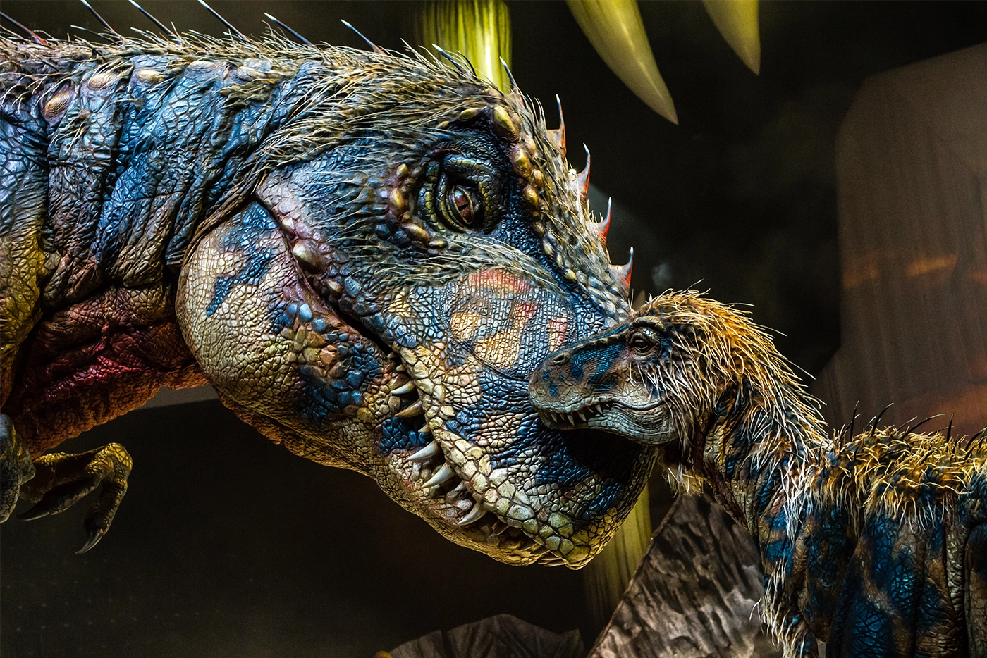 Two realistic dinosaur puppets from the Walking with Dinosaurs arena tour, featuring a large Tyrannosaurus rex and a juvenile nuzzling against it, with detailed textures, scales, and lifelike features.