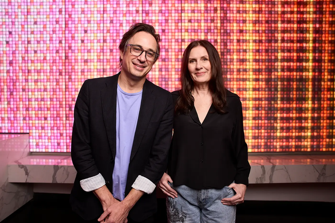 Producer Carmen Pavlovic and Creator Trent Dalton of Boy Swallows Universe in front of a pink and orange lit up led screen