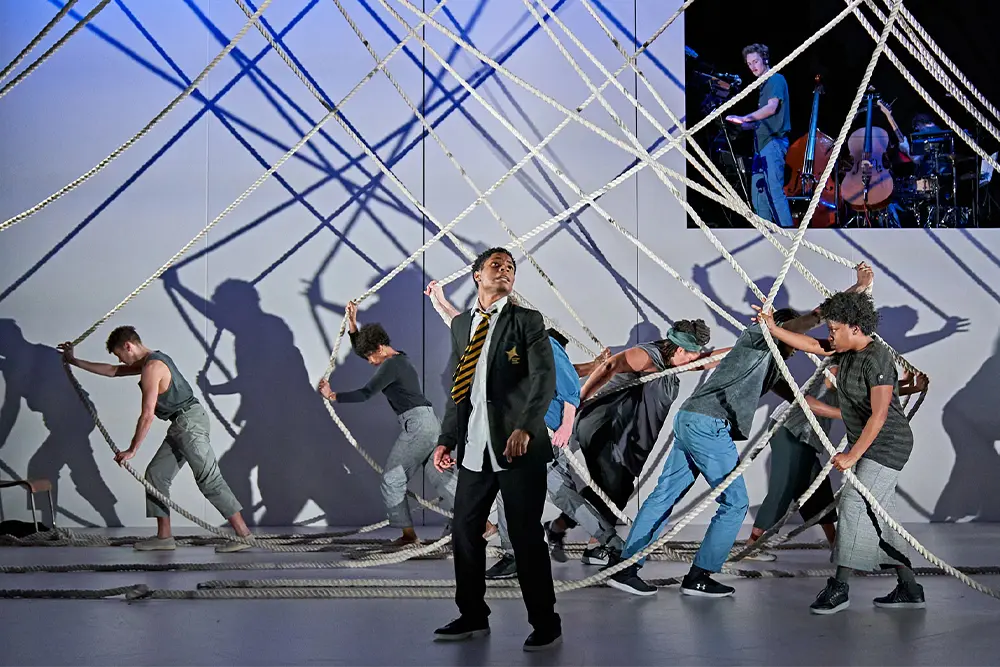 Production image from A Monster Calls. School kid infront of cast pulling ropes connected to the ceiling around
